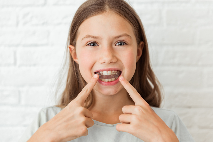 Attractive little girl shows index fingers myofunctional trainer. Help equalize the growing teeth and correct bite, develop mouth breathing habit. Corrects the position of the tongue